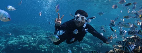 Man snorkeling with fish and holding up a peace sign