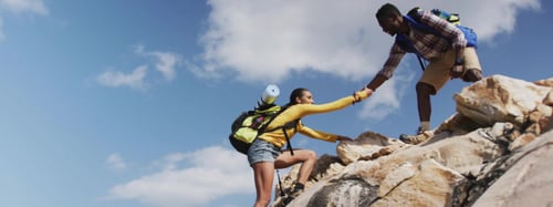 Man helping woman hike up a rock