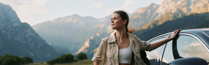 Woman standing beside a car with her hand on it in a mountain range