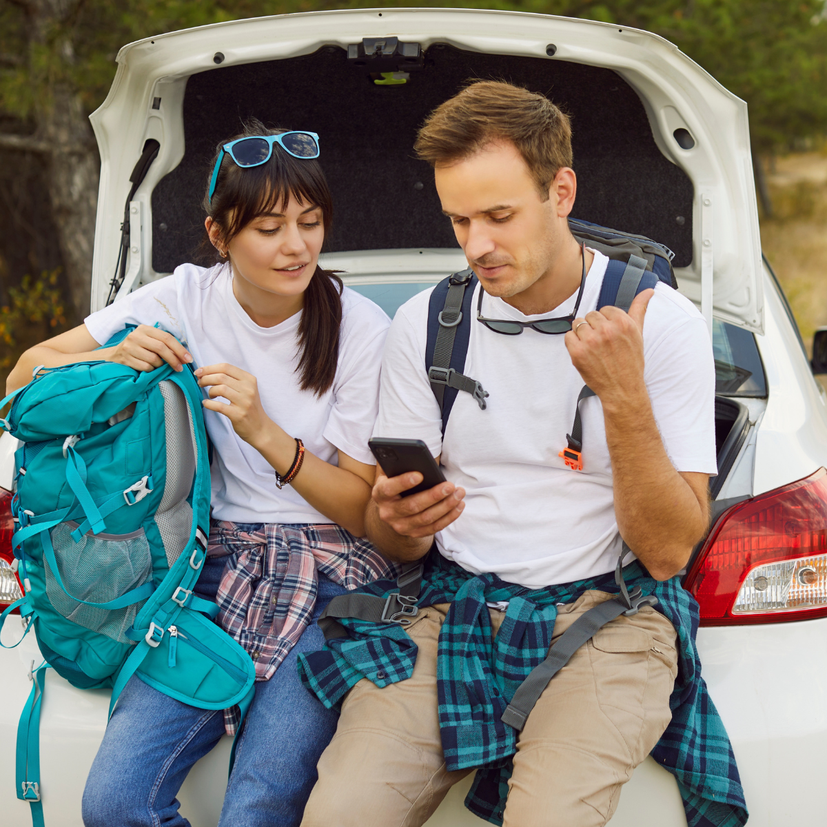 Couple sitting on the trunk of a car looking at a phone