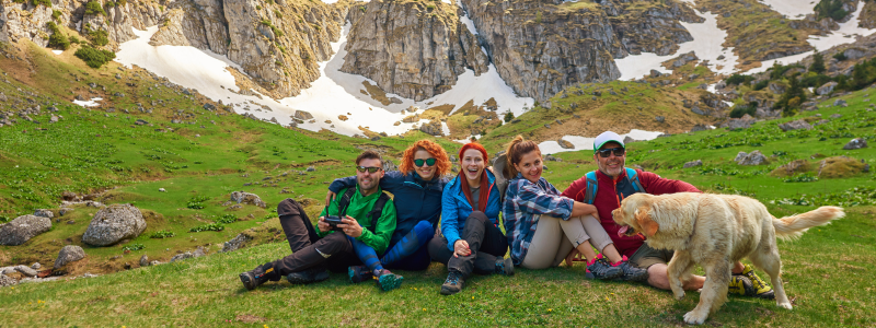 Group of 5 friends sitting together on grass with a dog
