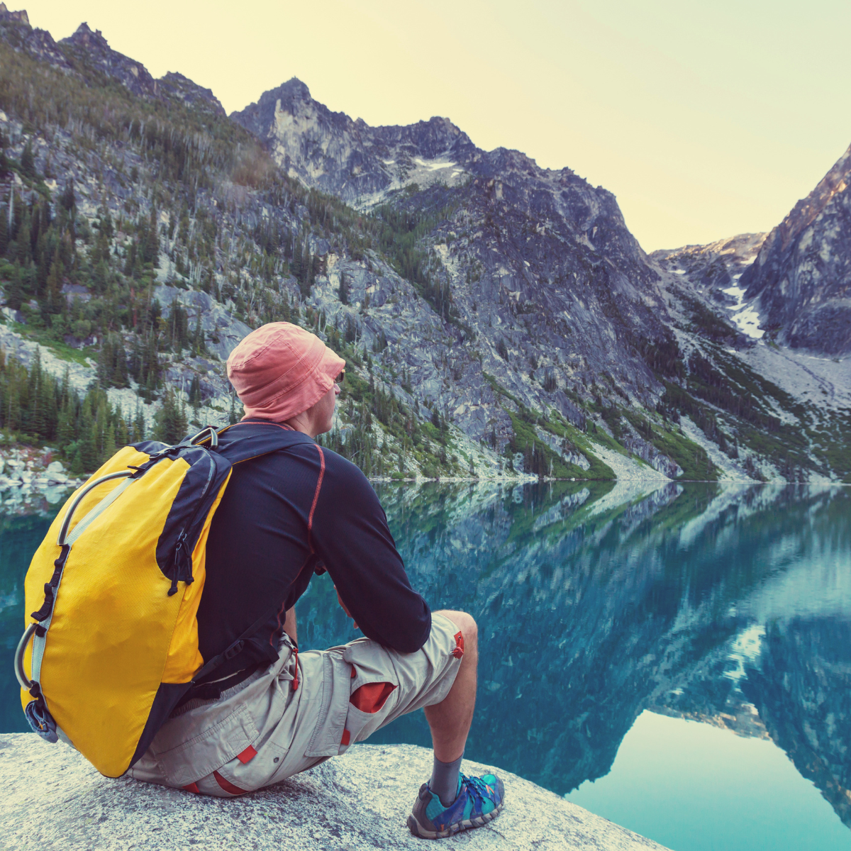 Man sitting on a rock looking into a mountain range over a lake