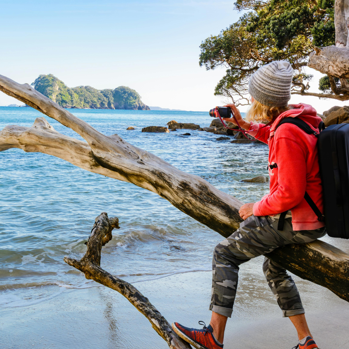 Man sitting on driftwood at the beach taking a picture of the ocean