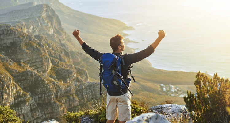 Man wearing a backpack standing on a cliff with hands in the air