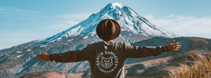 Man with his arms out facing away from the camera facing a mountain