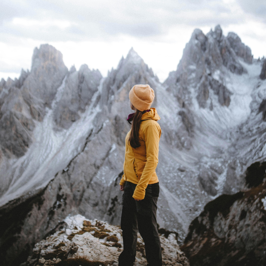 Woman in a yellow jacket looking into distance at mountains