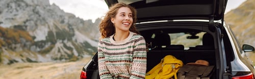Woman sitting against the trunk of a car smiling