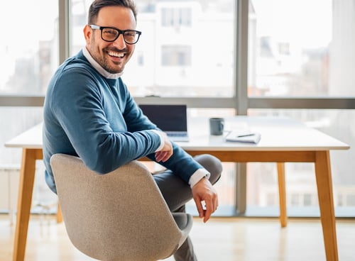 Man in a blue business suit sitting on a chair smiling