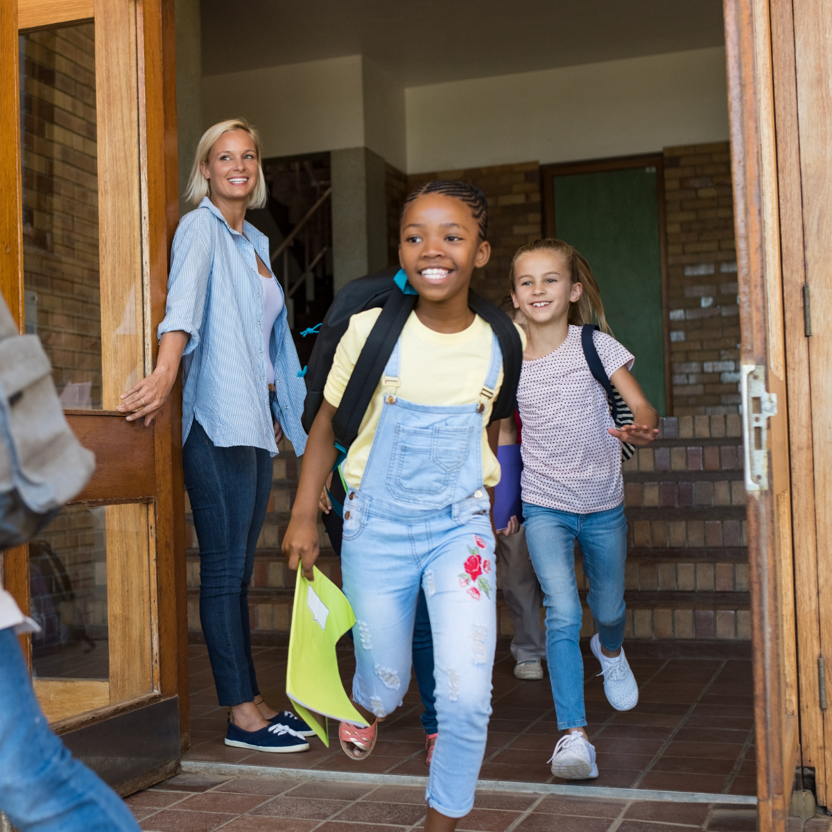 Kids running out of school with teacher opening doors behind them