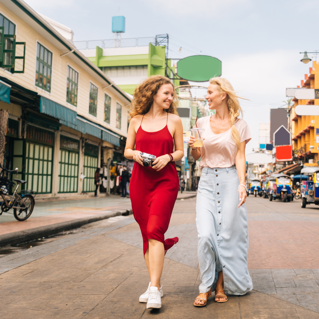 Two friends walking down a street together looking at each other