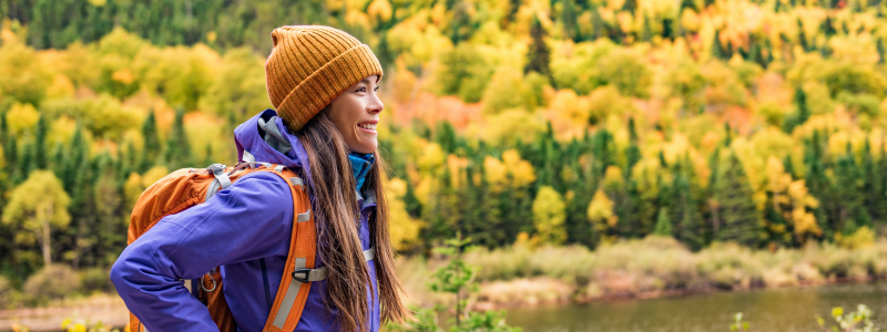 Woman wearing a beanie smiling into the distance amongst fall trees