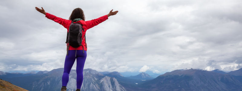 Woman standing with hands in the air and mountain range in the background
