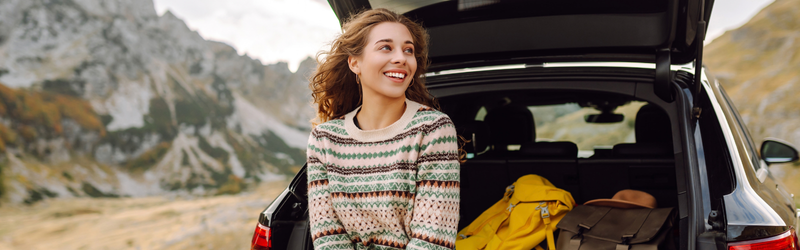 Woman sitting against the trunk of a car smiling