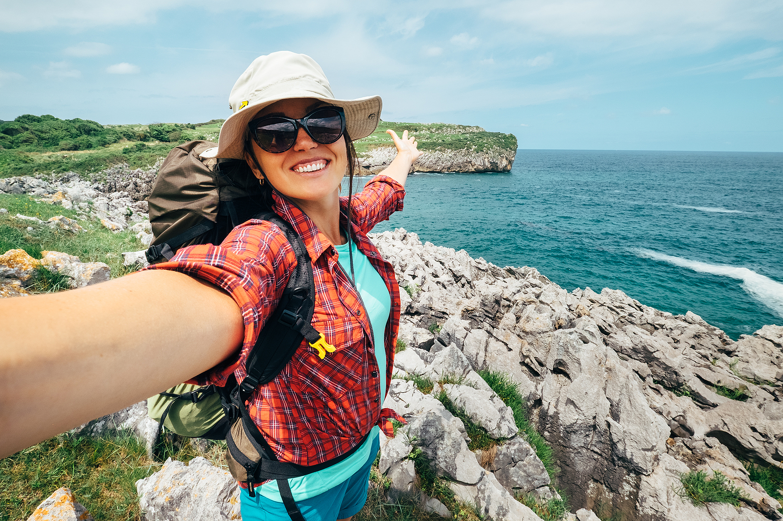 Lady taking a selfie while traveling while standing on rocks by the ocean